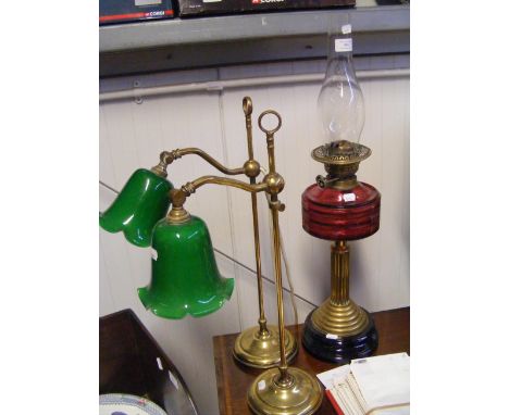 An antique oil lamp with cranberry glass, together with a pair of two green glass shade table lamps