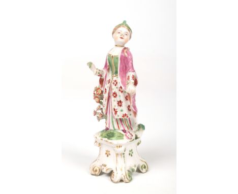 A rare Bow figure of a female Turk. Coloured in enamels, stood beside a spray of flowers and raised on a scrolling table base