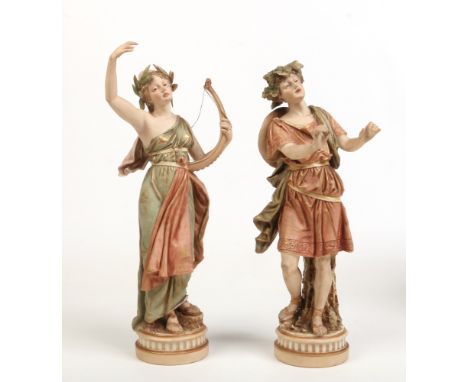 A pair of Royal Dux figures modelled as Grecian dancing figures. He wearing a toga with a vine wreath in his hair and his com