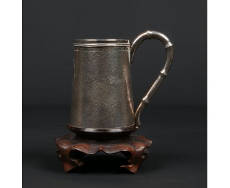 An early 20th century Chinese silver tankard of tapering cylindrical form on associated hardwood plinth. With textured ground