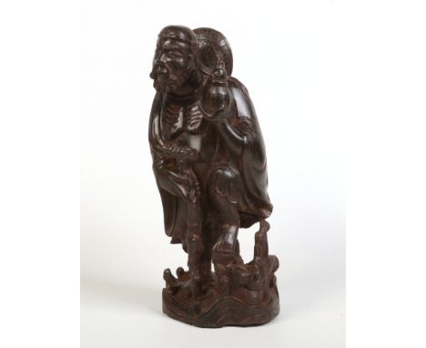 A Chinese carved hardwood sculpture of an Immortal. Supporting himself on a walking stick and holding a flask, 38cm high.Cond