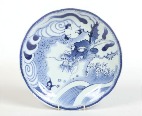A Japanese late Edo period blue and white dish. Boldly painted in underglaze blue with a dragon clutching a pearl on a cloud 
