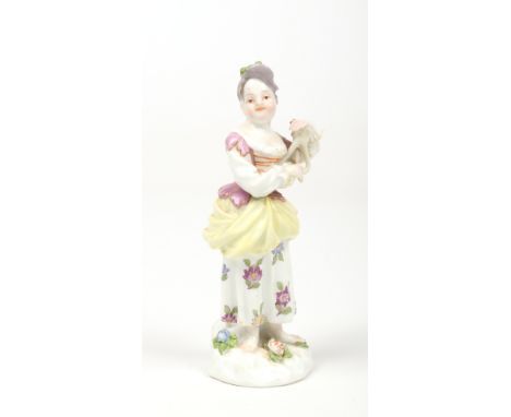 A Meissen figure of a female musician playing a triangle. Stood upon a rocky base applied with flowers. Feint underglaze blue
