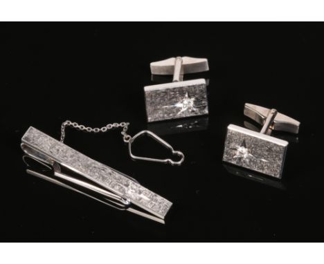 A 14 carat white gold tie clip and pair of cufflinks en suite. With textured grounds and each set with a brilliant cut diamon