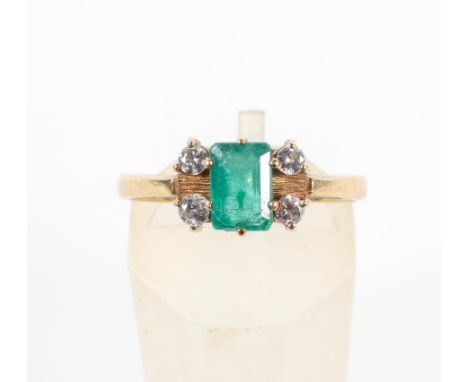 A yellow metal ring. Principally set with a rectangular cut emerald and finished with four round brilliant cut diamonds. Hall