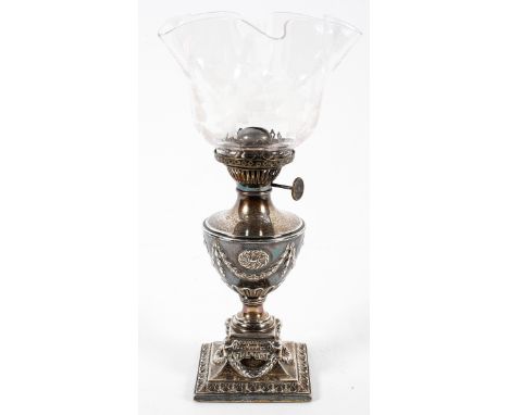 A Victorian silver urn shaped oil lamp and engraved glass lamp, late 19th century, cast with medallion and swags, on ram's he