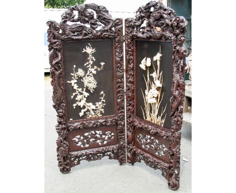 A Chinese hardwood carved two-fold screen, late 19th Century, the elaborate dragon and scroll carved frame securing ebonised 
