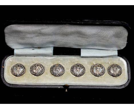 A cased set of six Edwardian silver buttons, each with embossed decoration of a figure in classical dress playing a lute type