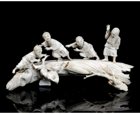 A 19th century carved ivory figure group, modelled as children playing on a realistically carved tree trunk, 27cm long