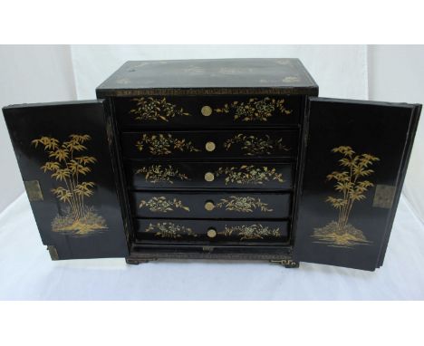 An Oriental lacquer table-top cabinet, the two panel doors opening to reveal five drawers with turned pulls and raised on sha