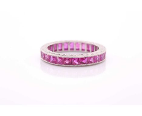 A ruby eternity ring, set with mixed faceted rubies, in a white metal mount with engraved decoration (unmarked, tests as plat