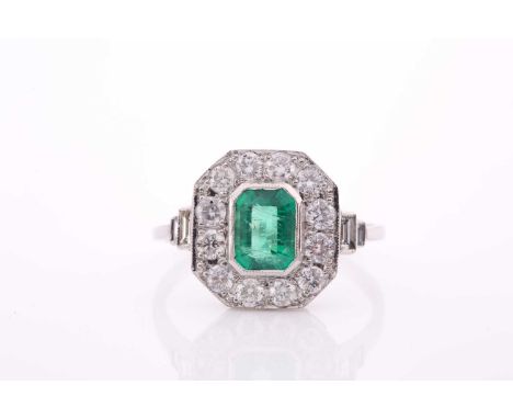 A platinum, diamond, and emerald ring, set with an emerald-cut emerald within a chamfered border of round-cut diamonds, ring 