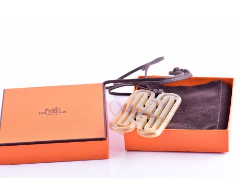 Hermes. A buffalo horn pendant, with carved patterned mount, 8 cm long, on a brown fabric necklace, in original box.