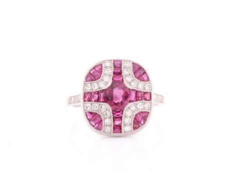 A platinum, diamond, and ruby ring, the rounded mount calibre-set with a mixed oval-cut ruby within a cross-designed mount of