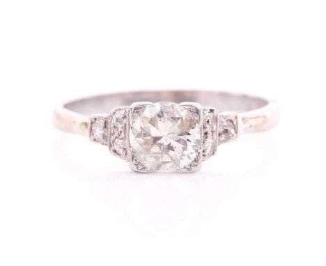 A diamond single stone ring; the round brilliant cut diamond in cornered claw mounts to three stone diamond shoulders in mill