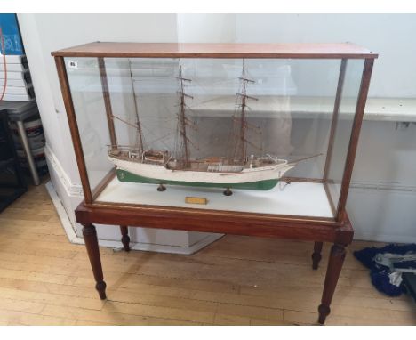 A painted wooden model in glazed display case of the USCGC Barque Eagle, on mahogany stand with round turned legs, overall he