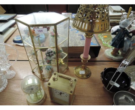 A glass display with ceramic posies, carriage clocks, candle stick