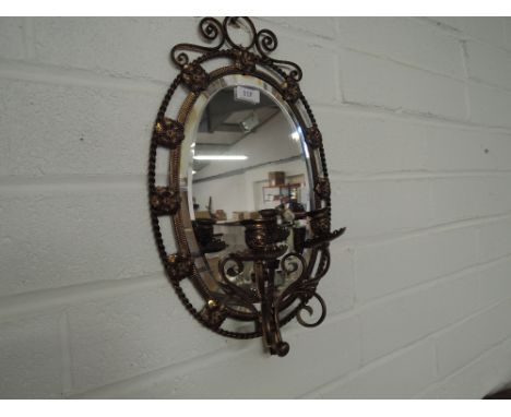 An oval wall mirror with  decorative surround and candle sconce