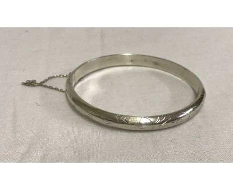 A 925 silver bangle with safety chain. Engraving to one side. Weight approx. 8.4g. Approx. 6cm internal diameter.