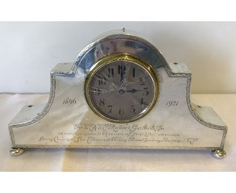 A silver cased mantle clock with engraving and bun feet. Engraving reads " 1896-1921 To Mr and Mrs Robert Gatecliff to commem