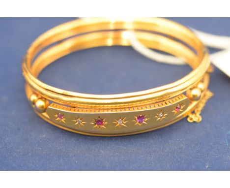 A yellow metal bangle stamped "9 CT", set with three diamonds and four rubies, 13.7grms.