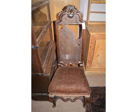 An 18th Century Jacobean style carved walnut hall chair, the high cane back decorated with leaf scrolls and flowerheads above