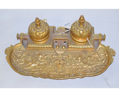 A gilded inkwell with embossed putti and scrolling decoration.