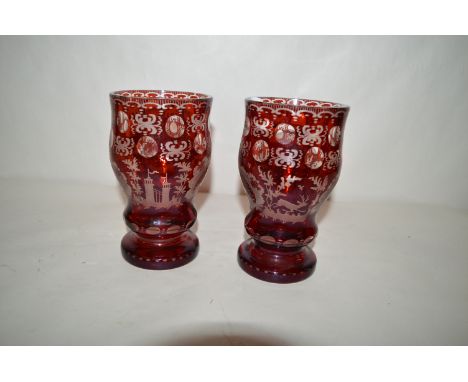 A pair of cut ruby glass Bohemian goblets, decorated with floral motifs, running stags and buildings.
