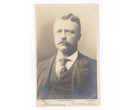 Theodore Roosevelt. A silver print postcard photograph portrait, the subject wearing a suit and tie, signed in lower margin '