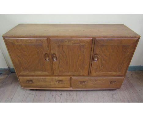 An Ercol Golden Dawn dining room cabinet of rectangular form fitted shelf and open deep cupboard enclosed by three doors over