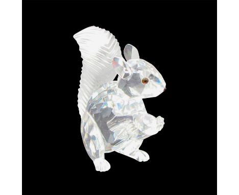 A clear crystal figurine of a squirrel with melon-colored eyes holding a diamond shaped crystal. Swarovski backstamp. This it