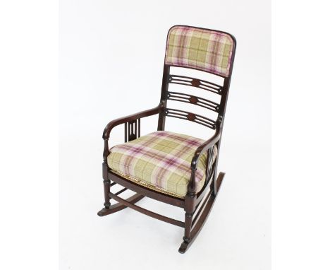 An Edwardian mahogany rocking chair, with a padded back rest above a pierced ladder back and a rattan seat, with bespoke fitt