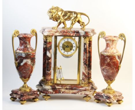 A late 19th century French rouge marble four glass clock garniture, the architectural marble case surmounted with a gilt meta