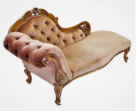 A Victorian walnut framed chaise longue, the shaped back with a carved crest extending to a leaf carved scrolling open work t