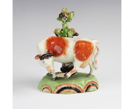 A Staffordshire pearlware cow in the manner of Obadiah Sherratt, early 19th century, modelled being bitten on the left rear h