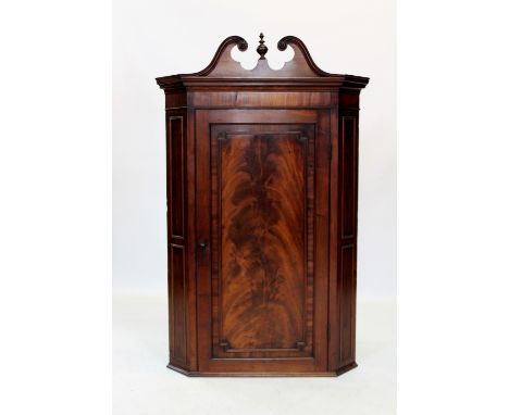A George III mahogany straight front hanging corner cupboard, the twin swan neck broken pediment centred with an urn shaped f