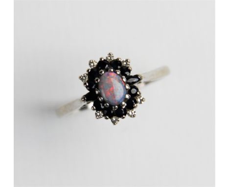 An opal, sapphire and diamond 18ct gold cluster ring, comprising a central oval opal cabochon measuring 6mm x 4mm, with a sur