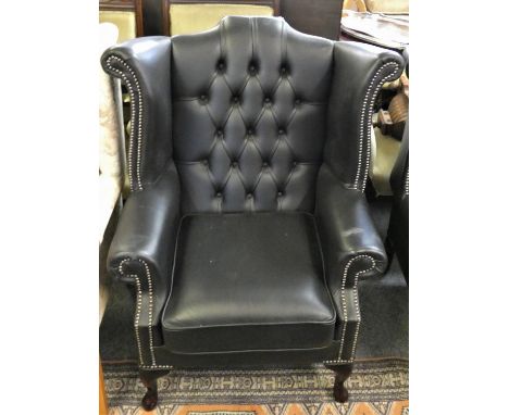 A black leather button back wing armchair 