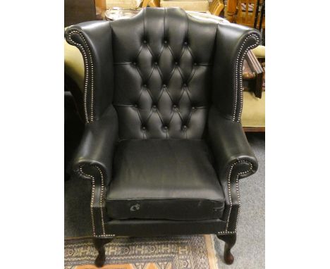 A black leather button back wing armchair 