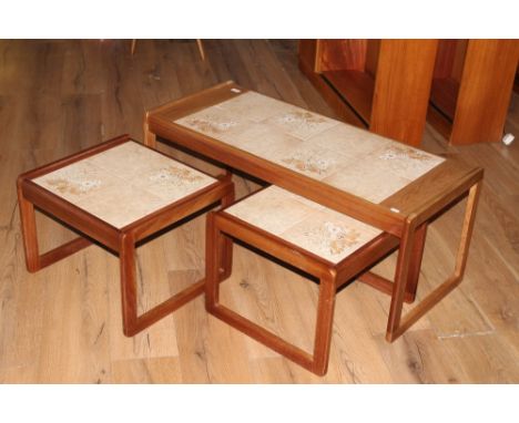 A nest of three 1970's tile topped teak tables, comprising one large rectangular table and two smaller square section tables.