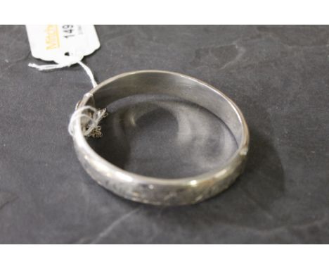 A modern silver bangle of hinged oval form with engraved decoration, inscription to the inner band, marked with lion passant 