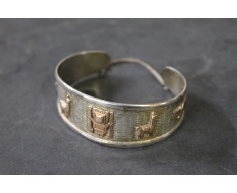 A Peruvian 925 grade white metal bangle with gold coloured highlights, mounded with South American designs, stamped 925 and 1