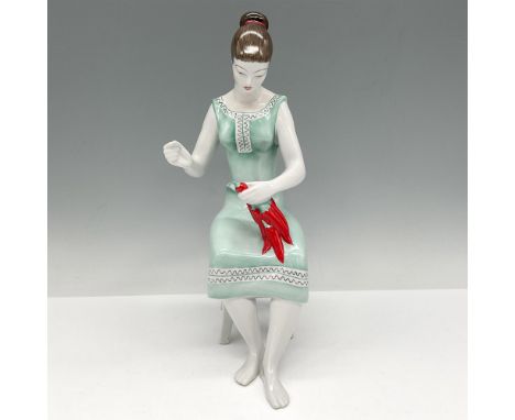 Figural sitting in chair wearing a pale green shift dress, holding a bunch of red chili peppers. Hollohaza backstamp. Issued:
