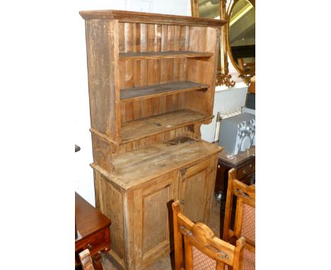 A stripped pine antique dresser with two panel doors and plate rack shelving above 