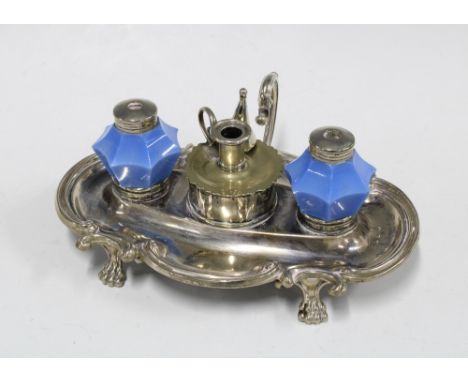 Epns desk inkwell with two blue glass wells and a candle snuffer to centre, standing on paw feet, 27cm long 