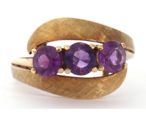 Amethyst set cross-over ring featuring three gold faceted cut amethysts between burnished and chased shoulders, stamped 585 (