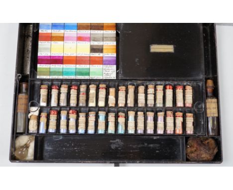 A black artist's tin box, with fitted interior, containing glass phialls of coloured shades of powdered paint and a white gla