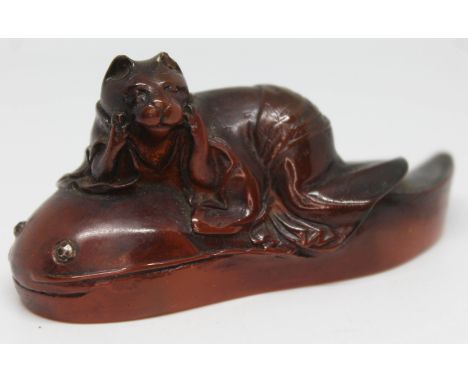 A Japanese carved amber coloured netsuke formed as a cat reclined upon a catfish, signature to base, length 8.5cm.Condition: 