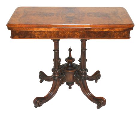 A Victorian walnut card table the hinged fold-over top on a fluted quadripartite scroll base joined by an urn finial, 92cm wi