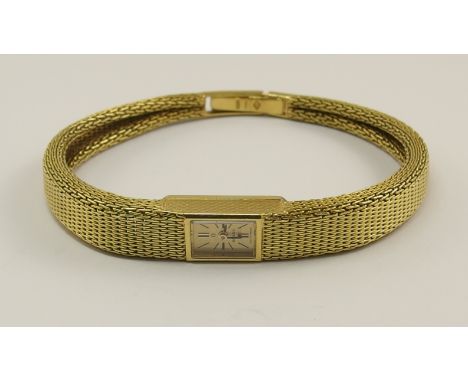 An 18ct gold ladies Omega wristwatch with small gold tone oblong face with black baton hands and numbers, with winder to the 